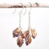 Sereia Sea Shell Dangling Earrings hanging on wooden stick